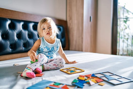 Little girl sitting on the bed with puzzle pieces in front of her. High quality photo