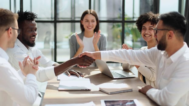 Glad to work with you. Young modern men in smart casual wear shaking hands and smiling while working in the creative office