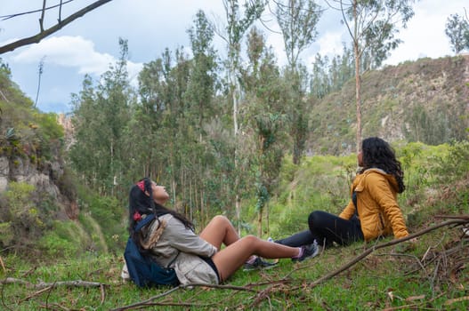 two Latin friends resting from a day of hiking and trails in Ecuador, sitting with their legs apart and looking at the sky. High quality photo