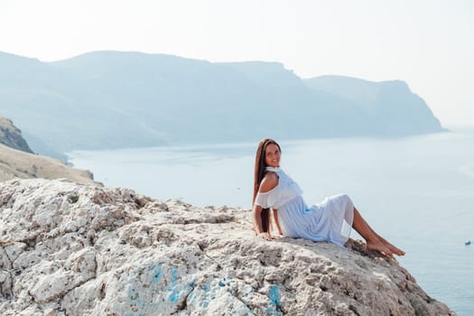 A woman with long hair in a dress looks at the landscape of the sea and rocks