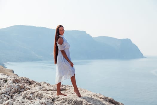 A woman with long hair in a dress looks at the landscape of the sea and rocks