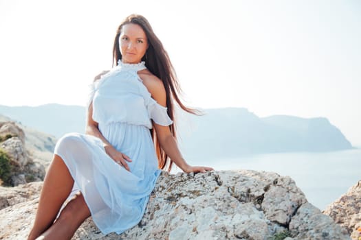 A woman with long hair in a dress looks at the landscape of the sea and rocks