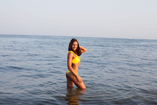 Beautiful tanned woman with long hair in yellow swimsuit sunbathes on the beach by the sea