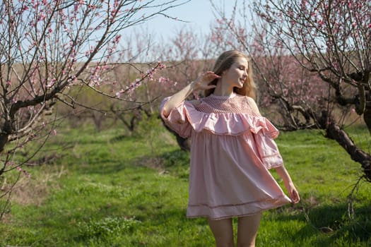 Beautiful woman in pink dress walks around the blossoming garden