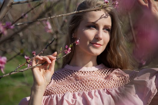 Beautiful woman in pink dress walks around the blossoming garden