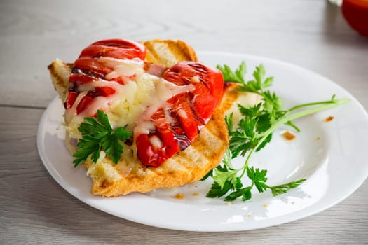 hot sandwich of fried toast bread with baked peppers and cheese, in a plate on a wooden table