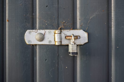 Old padlock, parts covered with rust, on gray wood fence.