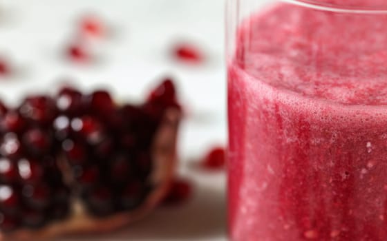 Detail on bubbles in pink smoothie, blurred pomegranate fruits in background