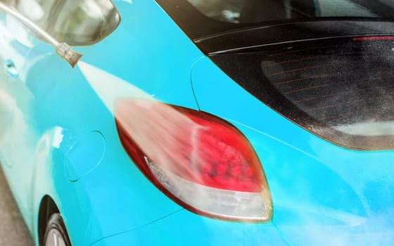 Rear light of blue car washed in self serve car wash, water spraying on the red surface.