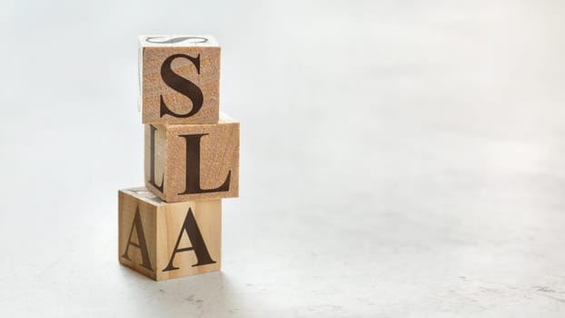 Pile with three wooden cubes - letters SLA meaning Service Level Agreement on them, space for more text / images at right side.