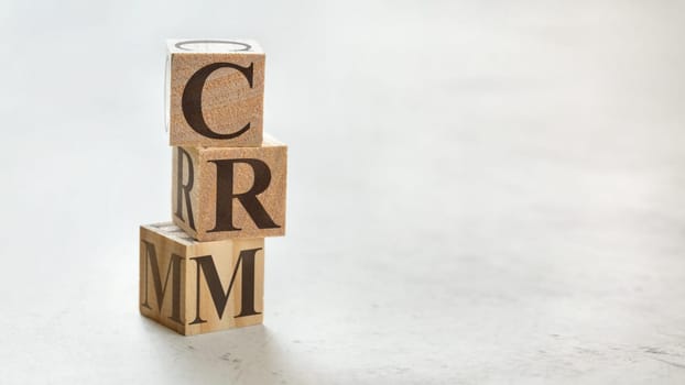 Pile with three wooden cubes - letters CRM meaning Customer relationship management on them, space for more text / images at right side.