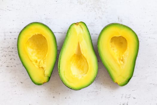 Three ripe avocado halves with bright yellow pulp on white working board, tabletop view