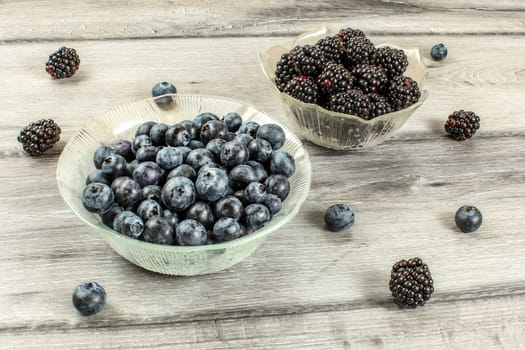 Small glass bowls with blueberries and blackberries on gray wooden desk.