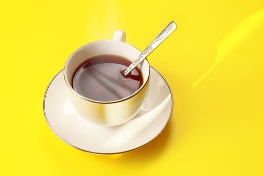 Morning sun shines to freshly brewed white porcelain cup of tea on yellow board table