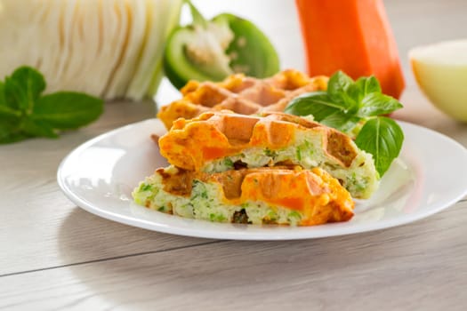 cooked two-color vegetable waffles made from cabbage and carrots, in a plate on a wooden table.