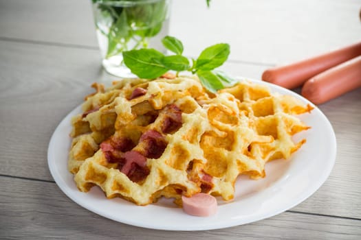 cooked fried potato waffles with sausage stuffing inside, in a plate on a wooden table.