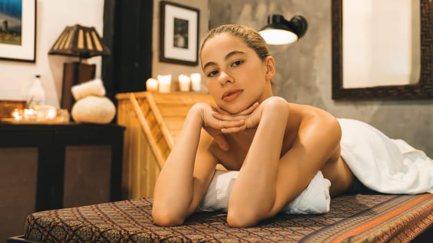 Portrait of beautiful caucasian woman in white towel woman lies on spa bed in front of warm wooden sauna cabinet with relaxation and peaceful at spa salon. Close up. A Side view. Tranquility.