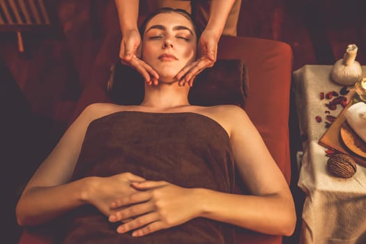 Caucasian woman enjoying relaxing anti-stress head massage and pampering facial beauty skin recreation leisure in warm candle lighting ambient salon spa in luxury resort or hotel. Quiescent