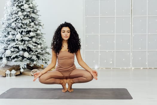 Beautiful brunette woman engaged in yoga fitness gymnastics asana near christmas tree