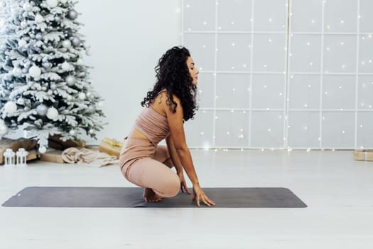 Beautiful brunette woman engaged in yoga fitness gymnastics asana near christmas tree