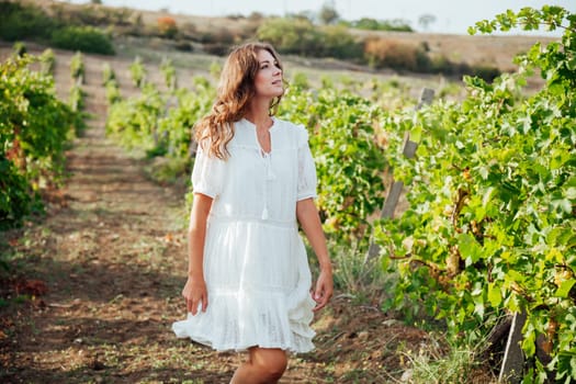 Beautiful woman in white dress collects grapes in the garden