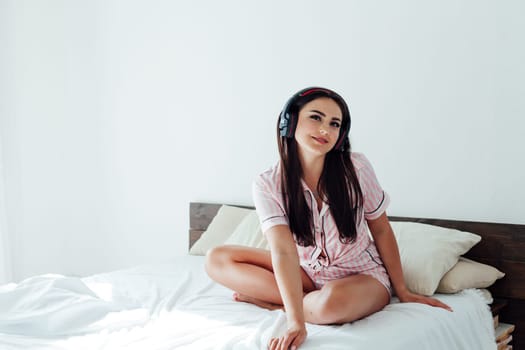 woman in pajamas in the bedroom on the bed listens to music with headphones