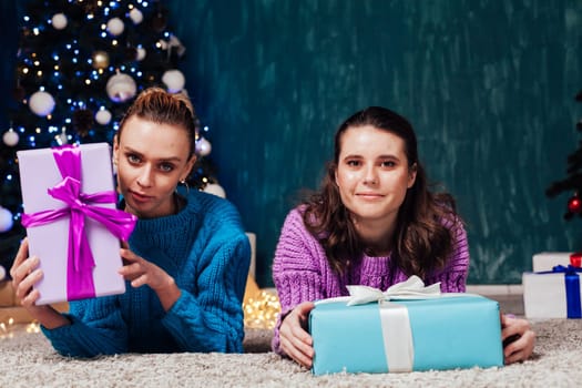 Two women with gifts at the Christmas tree for the new year