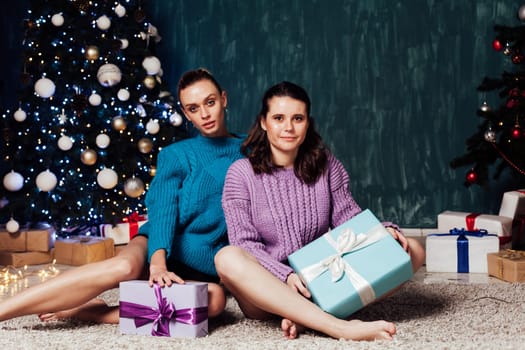 Two women with gifts at the Christmas tree for the new year