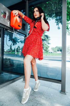 brunette woman in red dress talking in a phone booth