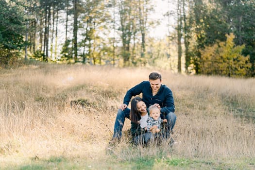 Dad sits behind mom with a little girl on his lap and strokes her head. High quality photo