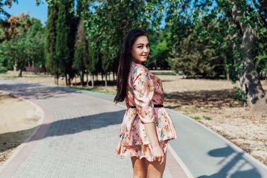 Beautiful athletic woman in dress with flowers walks in park alone