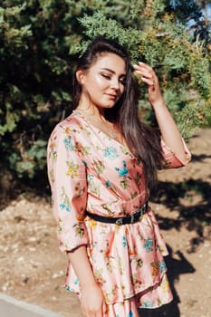 Beautiful athletic woman in dress with flowers walks in park alone