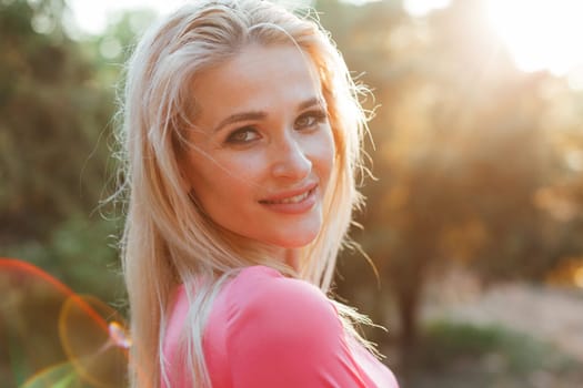 Beautiful woman in pink dress walks in the park at sunset