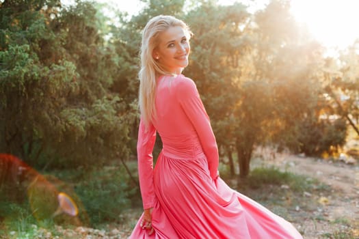 Beautiful woman in pink dress walks in the park at sunset