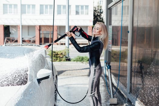 Beautiful female blonde driver washes car at car wash