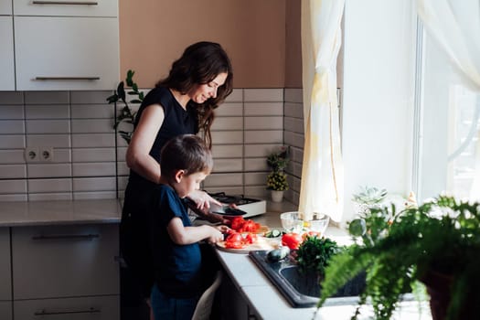 Mom and young son cut ripe vegetables for salad in the kitchen