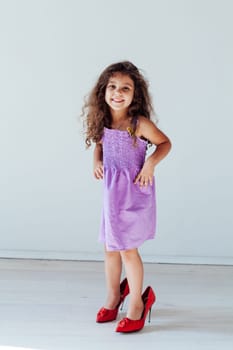 Little curly fashionable girl in a hat with fields and mom's shoes