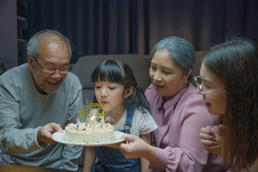 Birthday surprise. Happy Asian family grandparents and mother celebrating enjoy birthday party with cake of granddaughter at home in night time