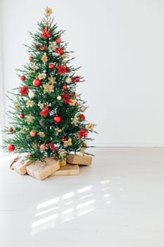 Big beautiful christmas tree decorated with beautiful shiny baubles and many different presents on wooden floor. White wall background with a lot of copy space for text. Close up.