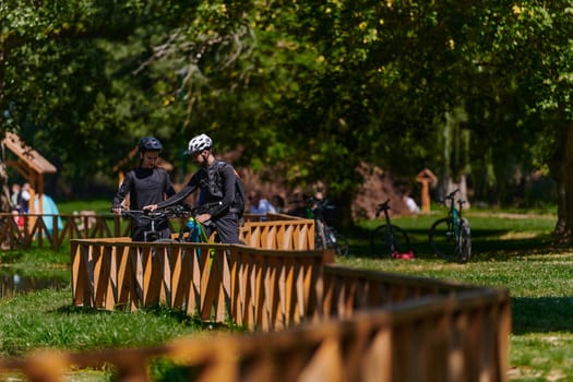 A blissful couple, adorned in professional cycling gear, enjoys a romantic bicycle ride through a park, surrounded by modern natural attractions, radiating love and happiness.