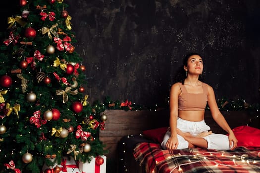 Beautiful brunette woman engaged in yoga asana on the bed near the Christmas tree New Year