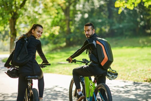 A blissful couple, adorned in professional cycling gear, enjoys a romantic bicycle ride through a park, surrounded by modern natural attractions, radiating love and happiness.