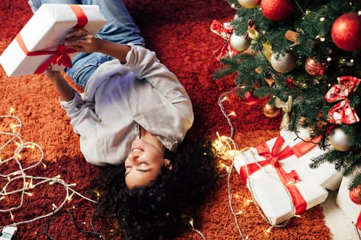 Beautiful woman lies near Christmas tree opens gifts for new year