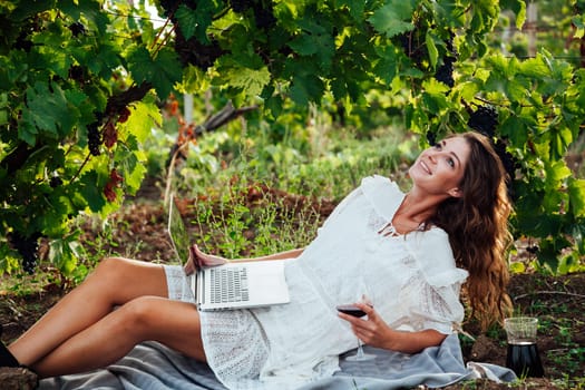 beautiful woman in white dress at a picnic with a laptop in the vineyards