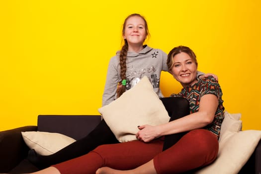 cheerful girl with mom at home on black sofa at yellow wall