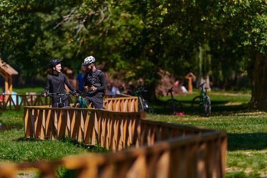 A blissful couple, adorned in professional cycling gear, enjoys a romantic bicycle ride through a park, surrounded by modern natural attractions, radiating love and happiness.