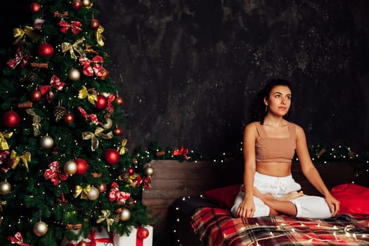 Beautiful flexible woman yoga asana on bed near Christmas tree New Year