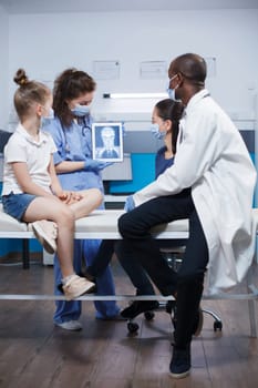 Healthcare worker and neurology practitioner analyze a digital display in a office. Patients, including a woman and child with a headache, receive medical advice and checkup with modern equipment.