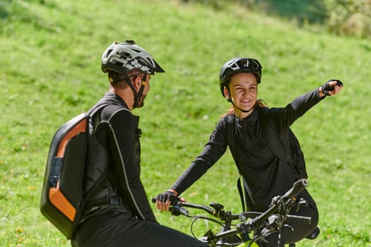 A sweet couple, equipped with bicycles and engrossed in coordinating their journey, checks their GPS mobile and watches while planning scenic routes in the park, seamlessly blending technology and outdoor adventure for a delightful cycling experience.