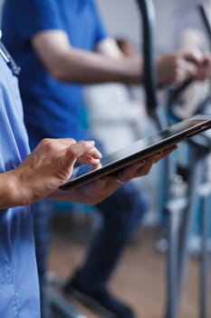Healthcare specialist in blue scrubs and a stethoscope is closely examining a patient report on a tablet in the hospital. Doctor is holding a digital device for conducting medical research.